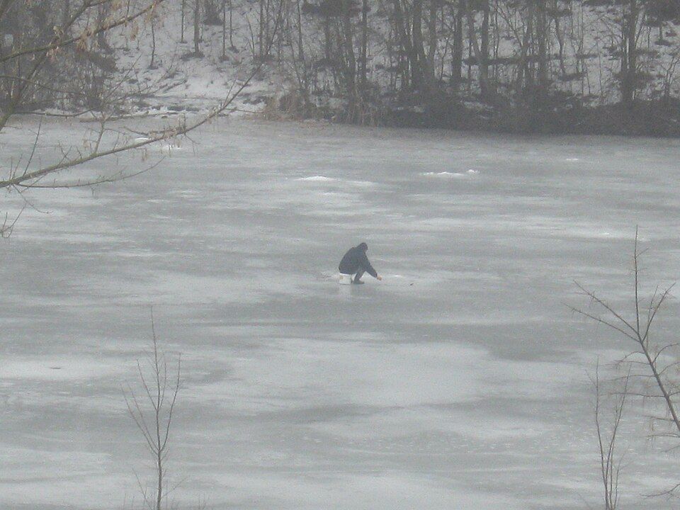 person ice fishing on frozen lake